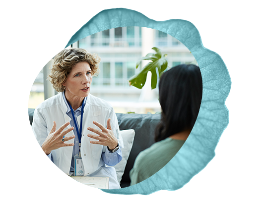 Wellness clinician in a white coat explaining treatment plan options and services to a patient with black hair and green shirt.